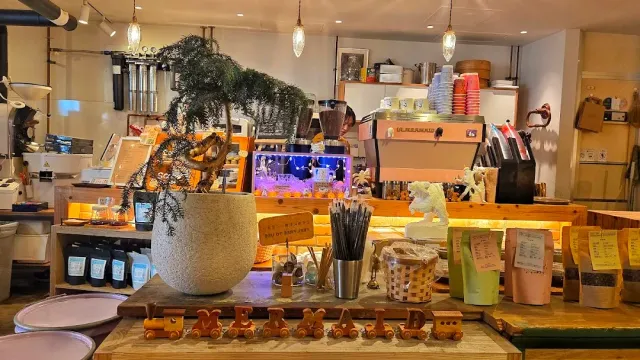 A counter loaded with coffee gear, a large potted plant, an espresso machine and wooden letters in front