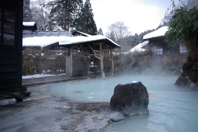 A steaming hot spring pool among rocks and snow
