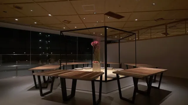 A dim room with wooden tables around a black metal frame holding a flower arrangement