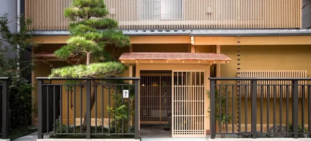 A building facade with a shaped pine tree, a wooden lattice gate and a black metal fence