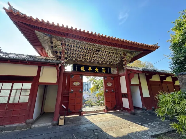 A red Chinese style gate with wood carvings beneath the roof and a gold inscribed plaque