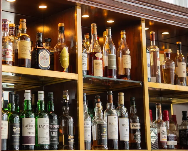 Lit wooden shelves packed with bottles of whisky and spirits