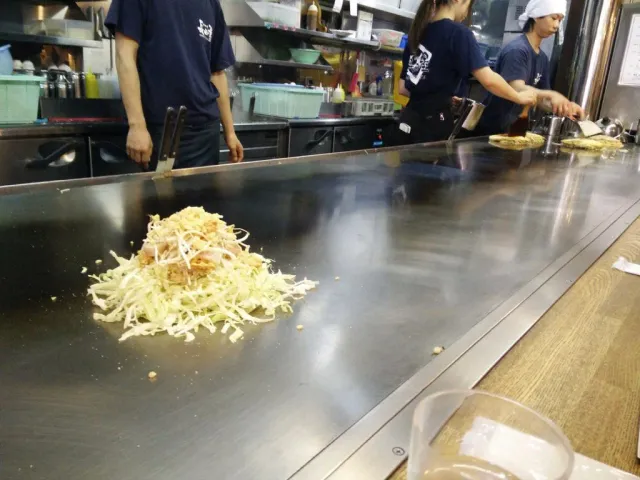Okonomiyaki cooking on a hot plate in front of chefs at the counter