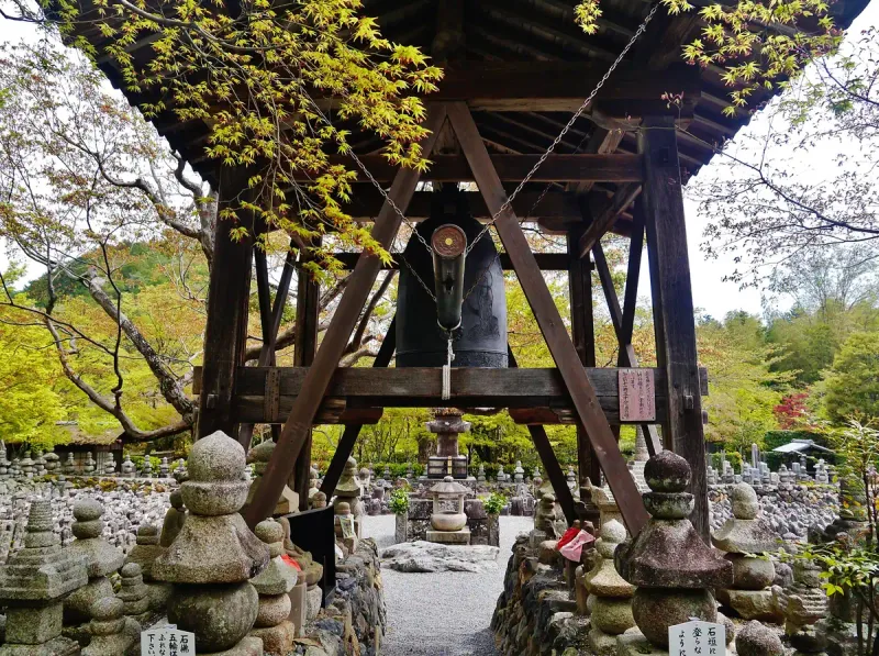 A wooden temple bell tower surrounded by hundreds of small stone memorials and spring trees