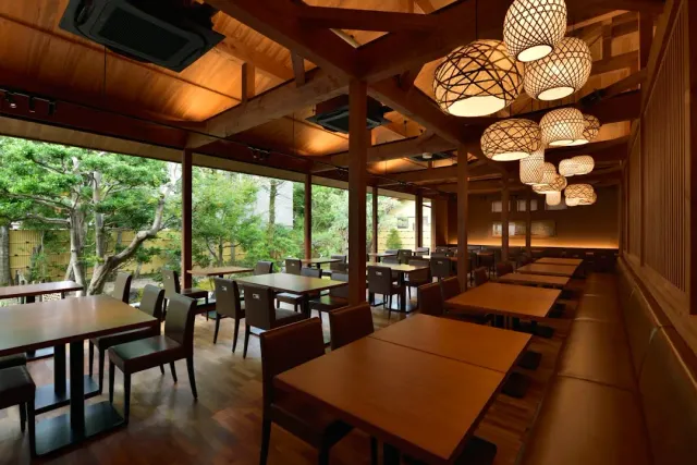 A spacious wooden hall with woven hanging lamps, tables and windows onto a green garden