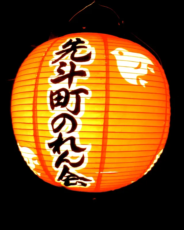 An orange paper lantern glowing with Japanese lettering at night