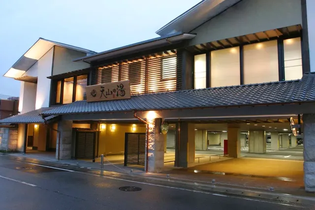 The facade of a wooden building with a tiled roof and a hanging sign, above a wet road at dusk