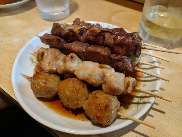 A plate of meat skewers in dark sauce on a wooden table
