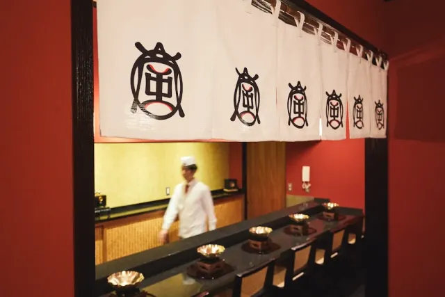 A white curtain with black emblems above a dark counter with wooden bowls, and a cook in white