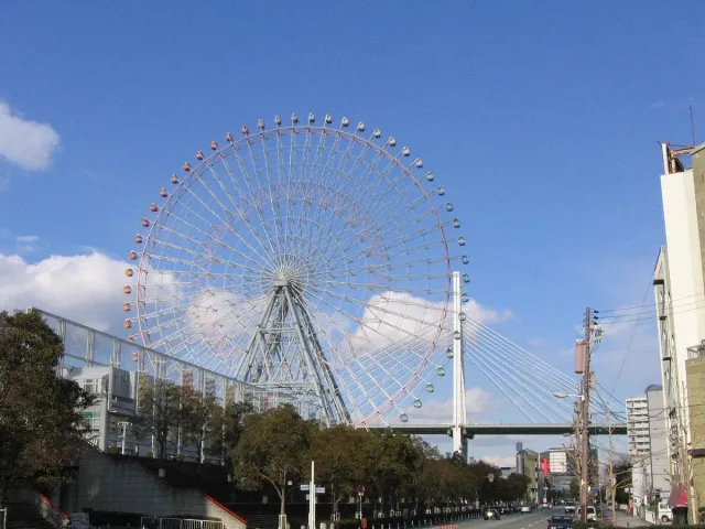 A large white ferris wheel against a blue sky beside a bridge