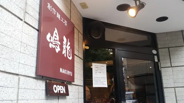 A burgundy sign with Japanese script above a glass entrance, and a small plate below it