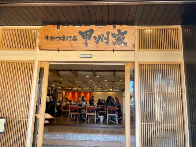 A wooden entrance with a large carved sign, and open doors onto a hall full of diners