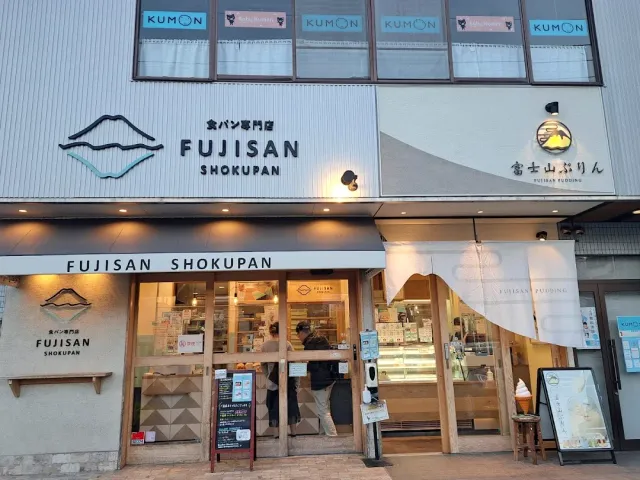 A building front with two signs and a mountain drawing, and inside people by a pastry fridge