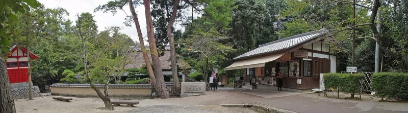 A museum compound with low wooden buildings, tall trees and visitors on the path