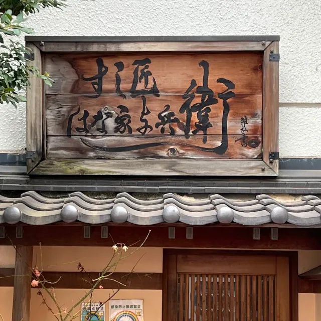A weathered wooden sign with black Japanese calligraphy, above a grey tiled eave