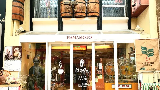 A front with a white sign, wooden barrels above the entrance and a display window full of objects