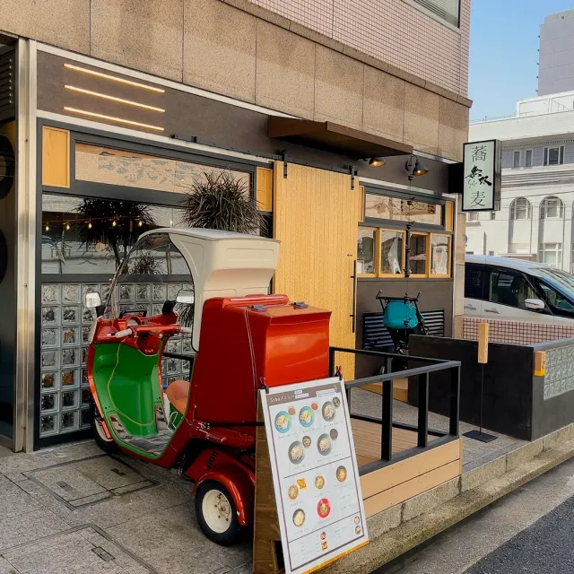A restaurant front with a red and green three wheeled scooter parked at the entrance and a menu sign
