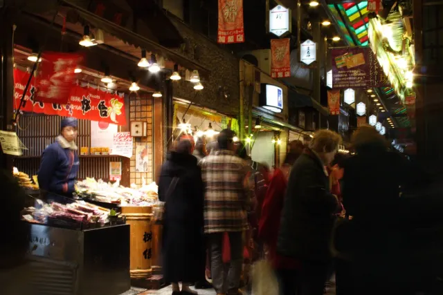 A covered market lane with lit stalls and shoppers