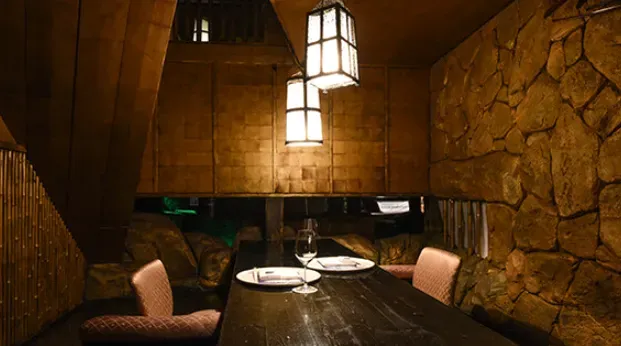 A dim space with stone walls, hanging paper lanterns and a wooden table set for two