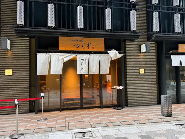 A dark brick frontage with a white fabric curtain, a wooden sign, hanging lanterns and a rope barrier