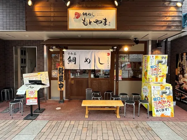 A frontage with a lit sign, a white fabric curtain, black stools and a wooden bench outside