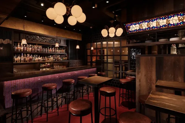 Leather stools at a long counter, globe lamps and a colourful stained glass window