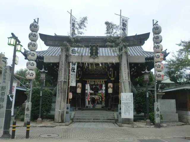 A wooden shrine gate with hanging lanterns and a stone gate in front