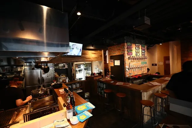 An open kitchen beside a bar counter with beer taps on a brick wall