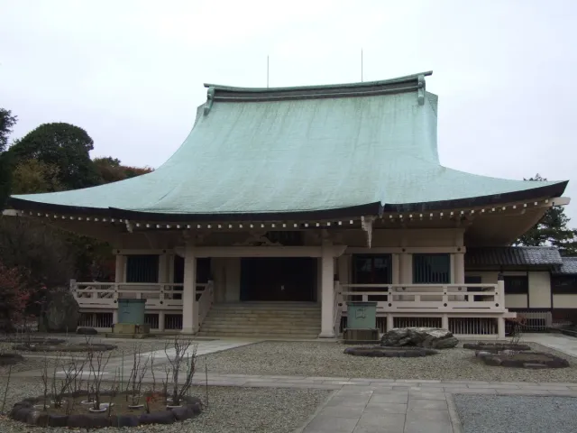 A wooden temple hall with a heavy tiled roof and a gravel courtyard