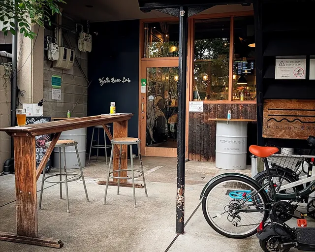 A tall wooden table with a glass of beer and stools in front of a glazed entrance