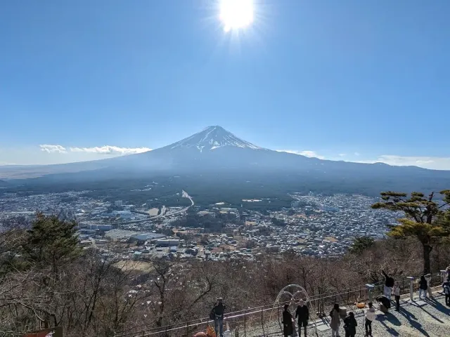 A snow capped conical mountain above a town, with visitors on a viewing deck in the foreground