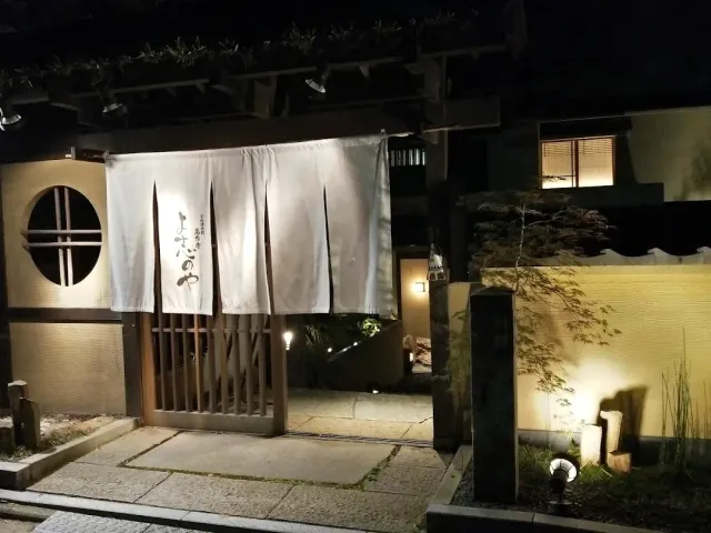 An entrance lit at night with a white fabric curtain, a wooden gate, a round window and a stone path