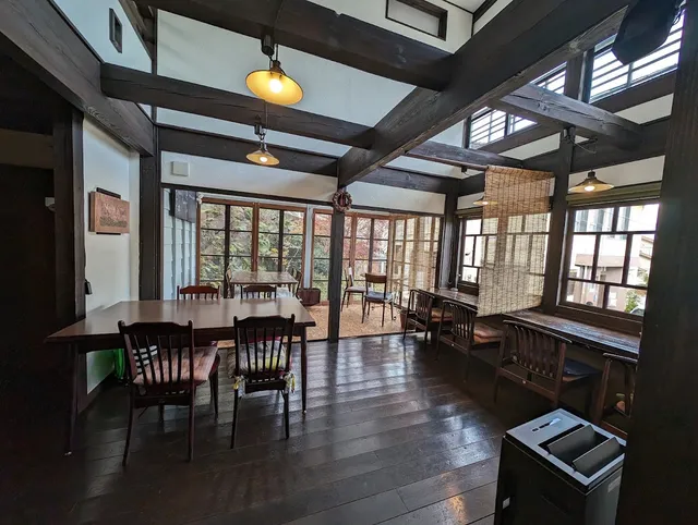A room with a dark wooden floor, exposed beams and many windows around the tables