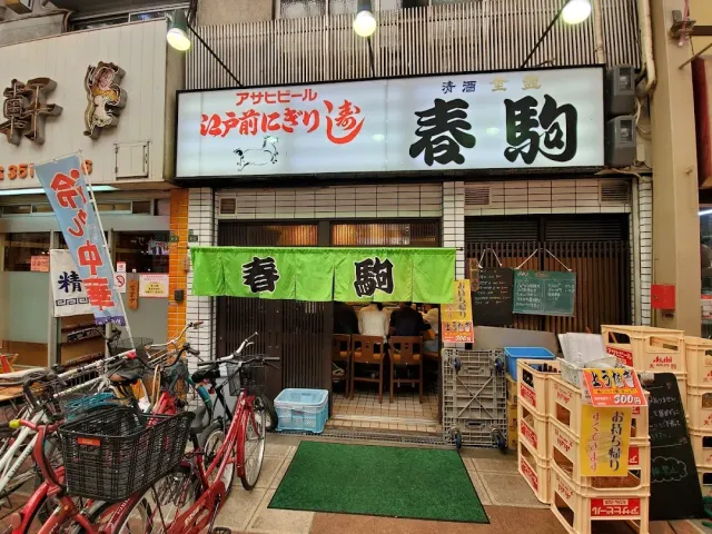 An entrance in a covered shopping arcade with a green curtain, parked bicycles and drink crates