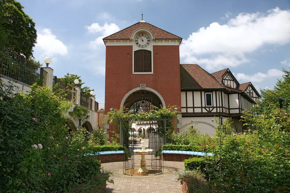 A rose garden with a fountain and an iron arch facing a red brick clock tower
