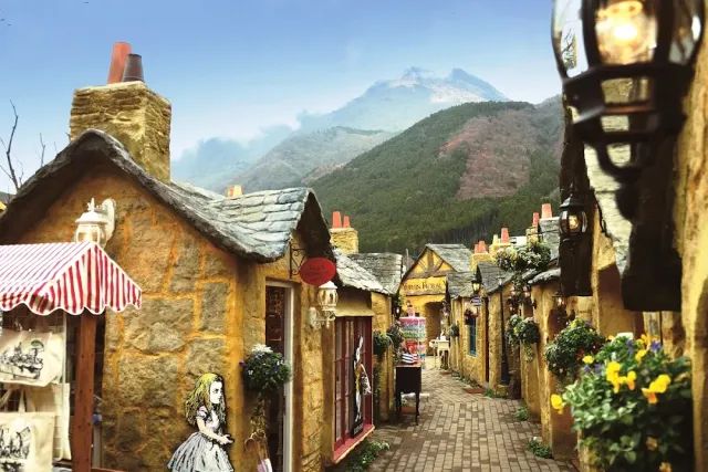 A stone alley with small stone cottages, flowers at the windows and a green mountain behind