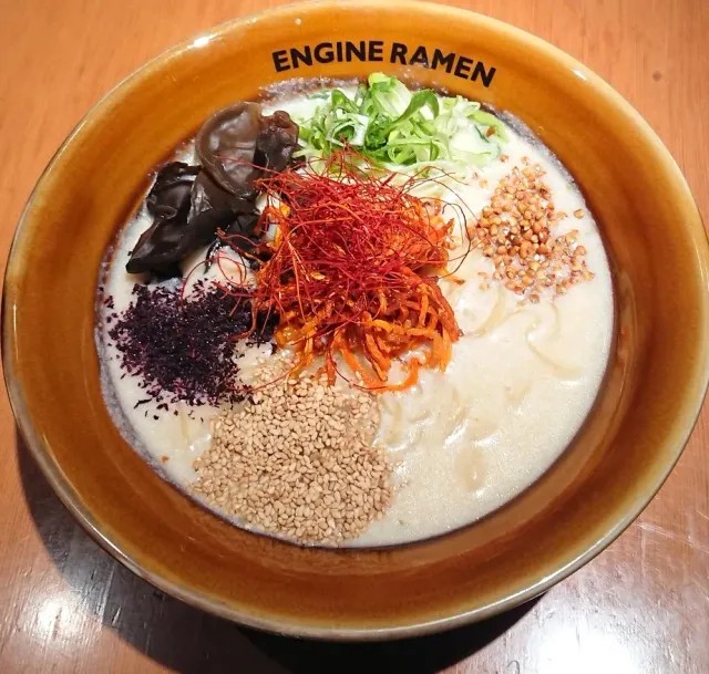 A bowl with thick white broth, red chilli threads, sesame, spring onion and mushrooms