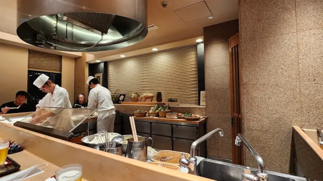 Cooks in white working behind a pale wooden counter, under a large metal hood
