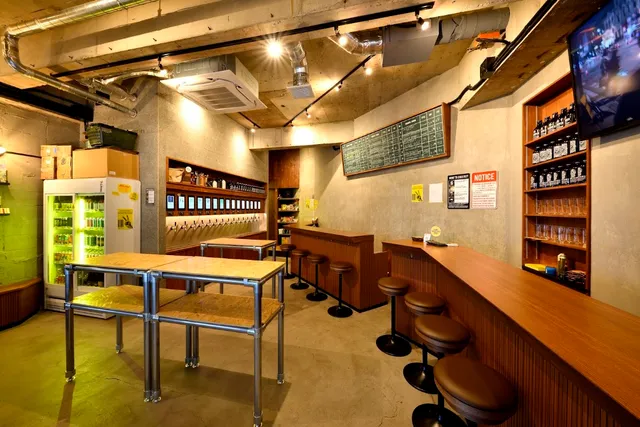 A wooden counter with stools, a wall of taps and a chalkboard in a lit concrete space