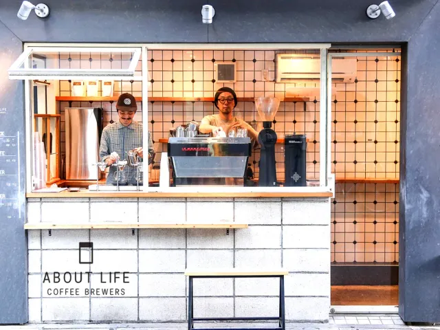 A serving window open to the street, two workers behind it and a coffee machine on the counter
