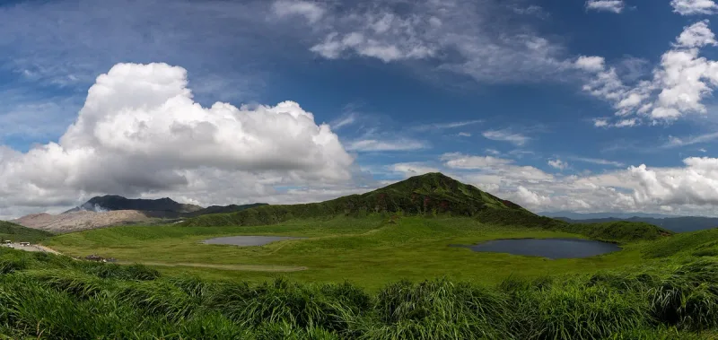 A green grass plain inside a dormant crater with two pools of water and a conical hill