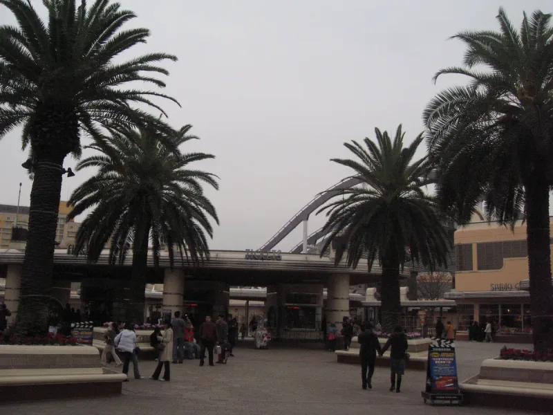 A theme park entrance plaza with a row of palms, a gateway and a crowd of visitors