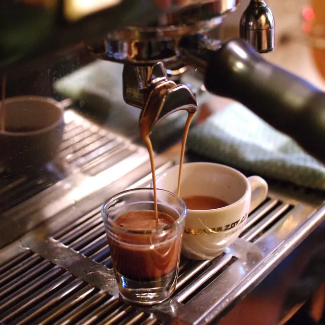 Espresso pouring from a machine into a shot glass and a white cup