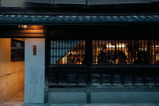 A traditional wooden building in the evening, with lit windows and diners seated inside
