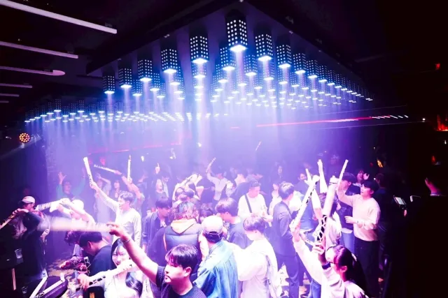 A dance floor full of people with glow sticks under purple light beams