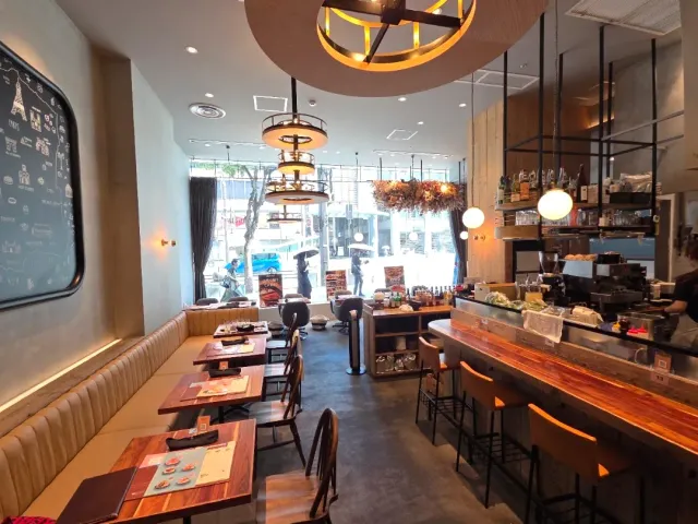 A polished wooden counter with stools, an upholstered bench and tables facing a shop window