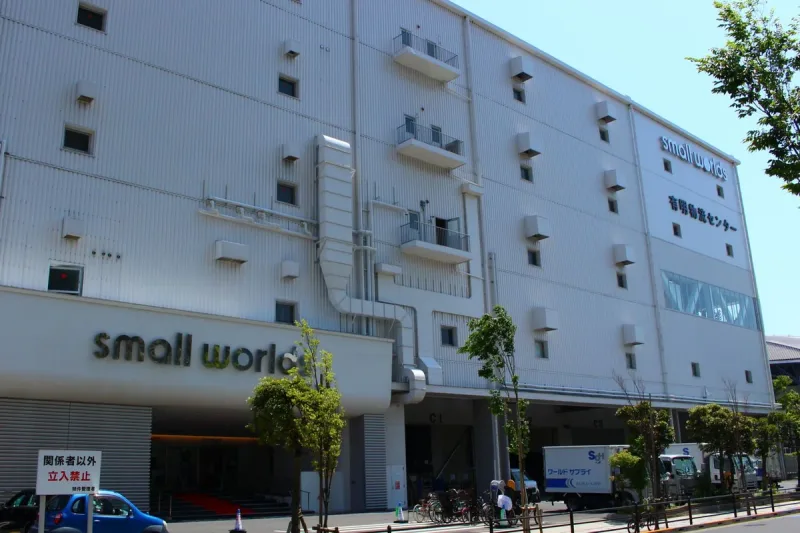 A white building frontage with a small worlds sign and a tree lined street in front