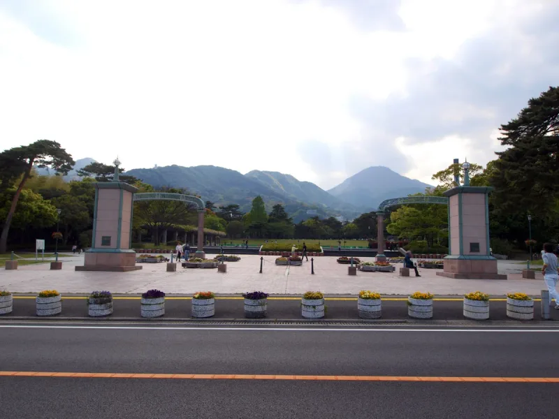 A paved plaza in a park with stone pillars, shrubs and a mountain ridge on the horizon