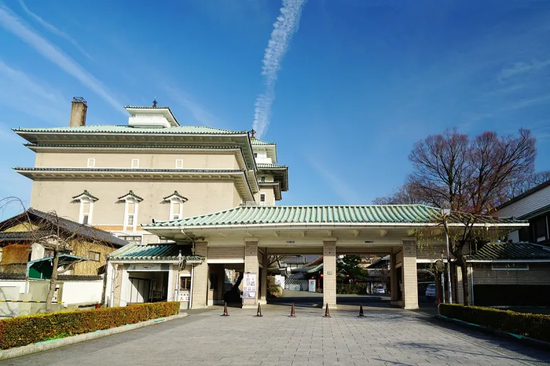 A theatre building with a green tiled roof, a covered entrance and trees in front
