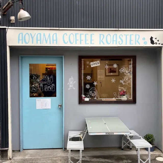 A grey facade with a light blue door, a painted window and a folding table outside